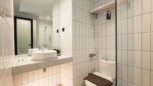A modern bathroom with white tiles, a glass shower enclosure, a double sink vanity, and a toilet. - ASSA Hotel Semarang (Semarang)