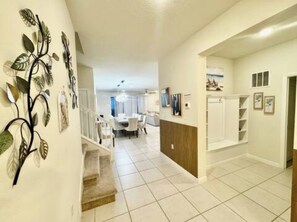 A spacious hallway with a staircase leading to a dining area, white walls, and a tiled floor. - The Disney Mansion by Orlando (Davenport)