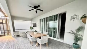 Ein moderner Essbereich mit einem Holztisch und weißen Korbstühlen, einem Deckenventilator und einer großen Schiebeglastür, die auf einen Balkon führt.