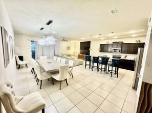 A modern kitchen with dark cabinets, a central island, and a dining area with white chairs and a large table. - The Disney Mansion by Orlando (Davenport)