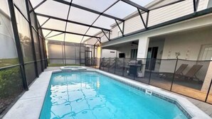 Ein rechteckiger Swimmingpool mit Glasveranda, umgeben von einer weißen Terrasse und einem Metallzaun.