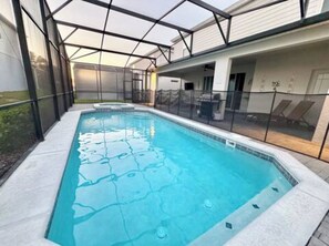 A rectangular swimming pool with a glass enclosure, surrounded by a white deck and a metal fence. - The Disney Mansion by Orlando (Davenport)