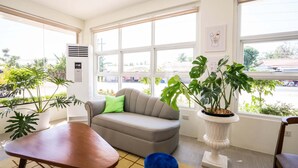 A modern living room with a grey sofa, a wooden table, and large windows offering a view of the street.
