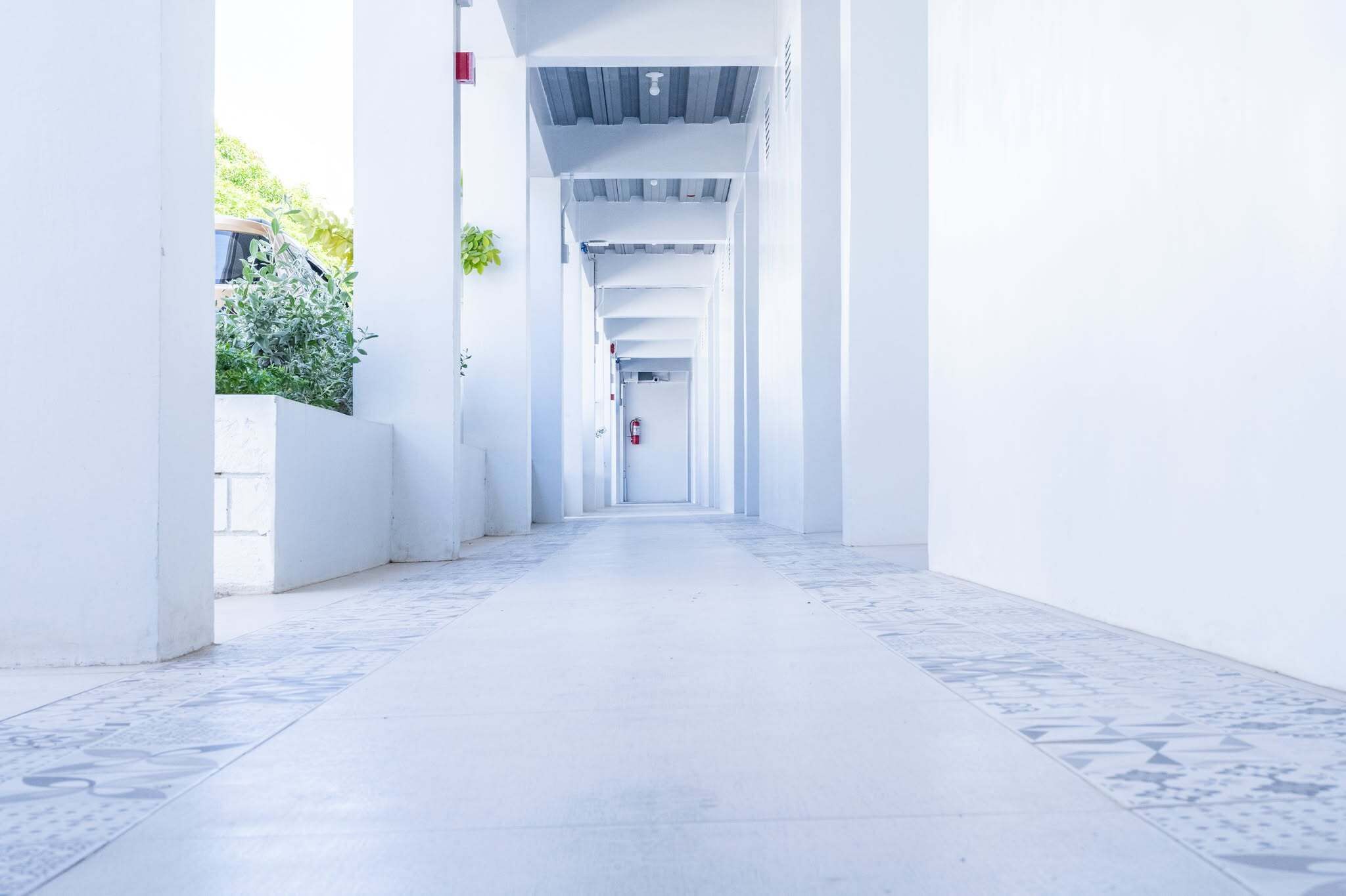 Un long couloir étroit aux murs blancs et au sol recouvert de carreaux décoratifs, qui mène à un extincteur situé au bout.