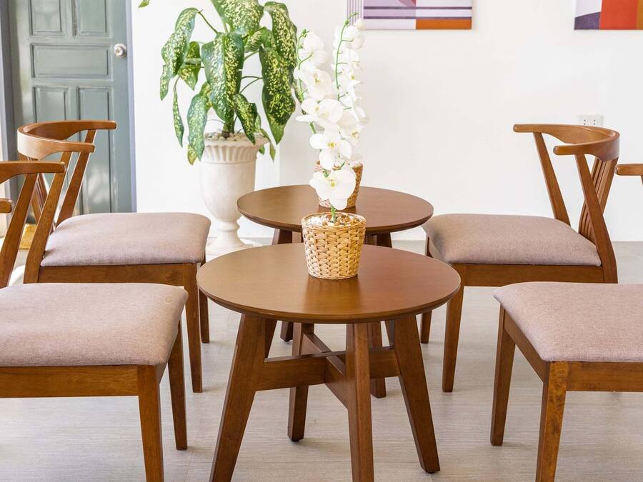 A dining area with wooden chairs and tables, a potted plant, and a door in the background.