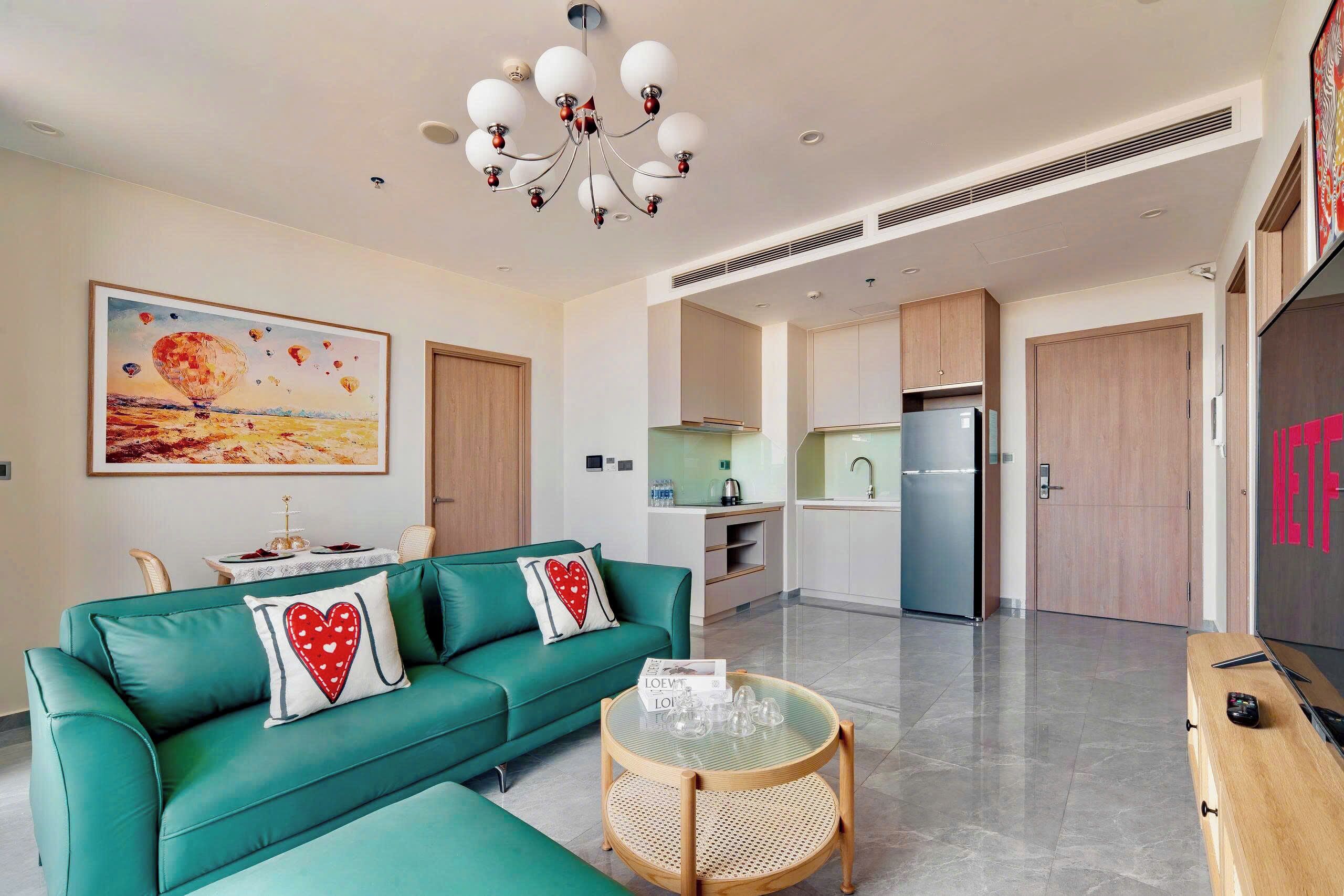 A modern living room with a teal sofa, a glass coffee table, and a chandelier.
