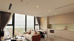 A modern living room with a large window, a sofa, a dining table, and a kitchen area.