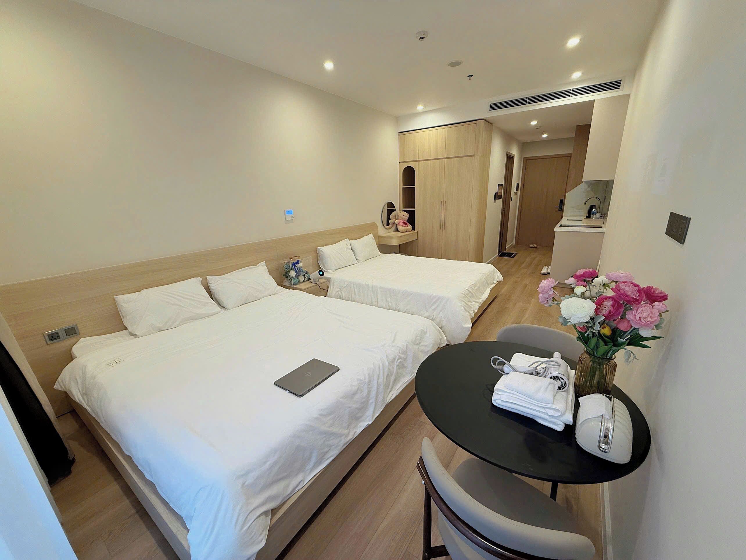 A hotel room with two beds, a small table with a vase of flowers, and a desk with a computer.