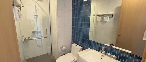 Un baño moderno con ducha envuelta en vidrio, inodoro blanco, lavabo grande y espejo con detalles de azulejos azules.