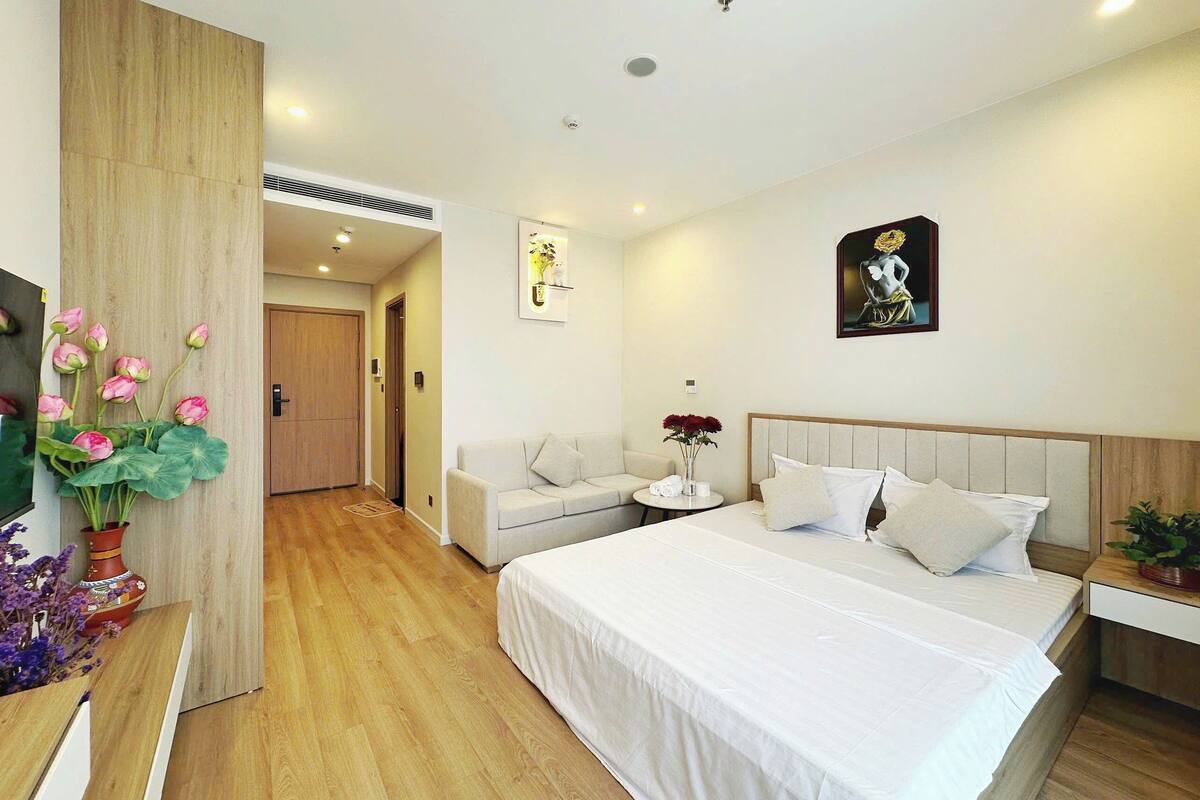 A hotel room with a large bed, a sofa, a small table with a vase of flowers, and a painting on the wall.