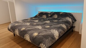 A modern bedroom with a bed, wooden flooring, and a wall-mounted light fixture. - House and studio with jacuzzi and private pool (Le Tampon)