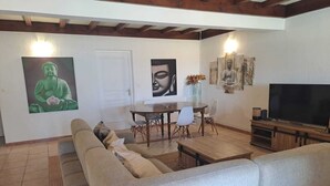 A living room with a sofa, a dining table with chairs, a TV, and artwork on the walls. - House and studio with jacuzzi and private pool (Le Tampon)