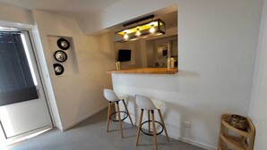A modern kitchen with a bar area, two white bar stools, a wooden sideboard, and a small wooden shelf with a bowl. - House and studio with jacuzzi and private pool (Le Tampon)