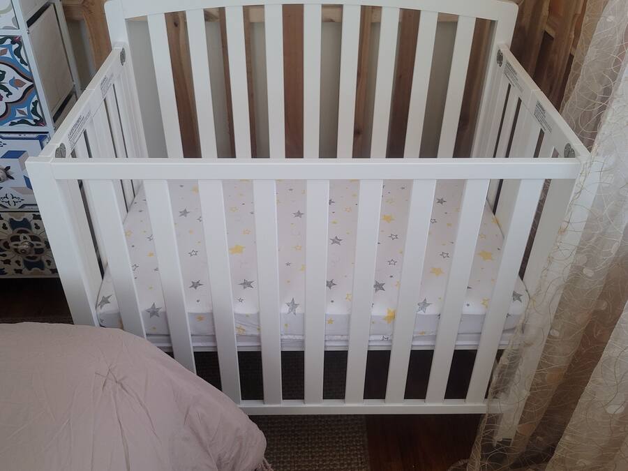 A white crib with star-patterned bedding, a pink pillow, and a woven rug on a wooden floor.
