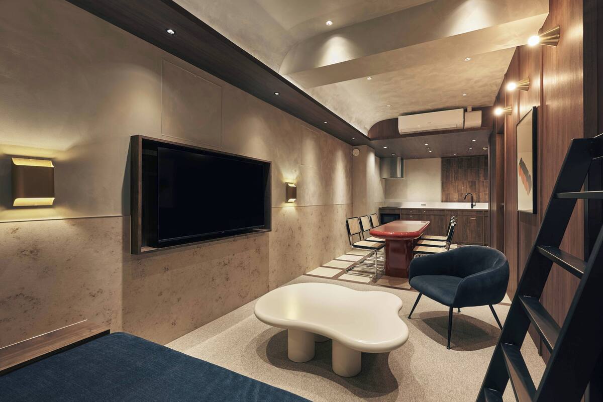 A modern interior with a flat-screen TV, a dining area with chairs, a unique white bench, and a staircase.