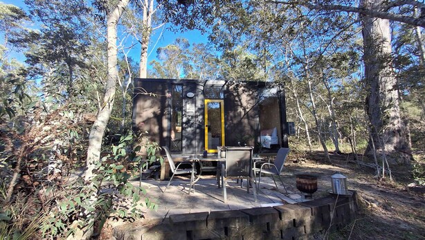 Une petite cabane avec une seule porte, une table et des chaises à l’extérieur.
