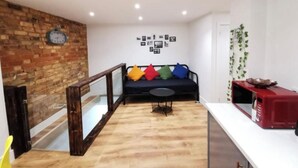Una sala de estar moderna con un sofá negro, cojines coloridos, una mesita redonda y un microondas rojo sobre una encimera blanca.