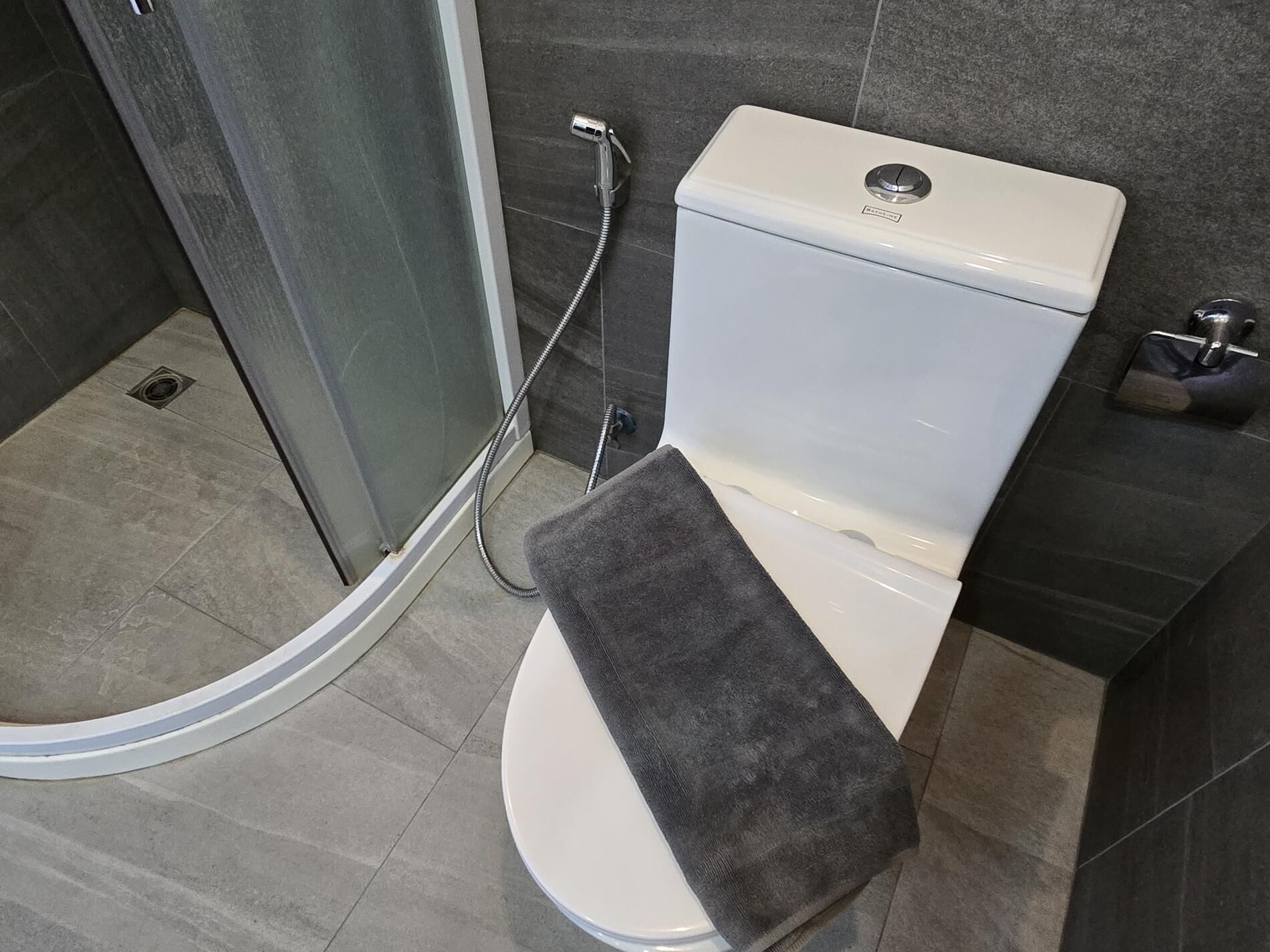 A modern bathroom with a toilet, a shower enclosure, and a towel rack.