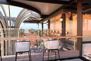 A modern bar area with two chairs, a glass railing, and a view of the outdoor seating area. - FTE Ha Long Hotel (Ha Long)