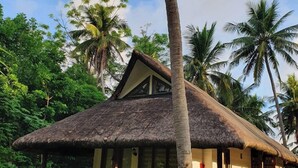 A thatched-roof bungalow with a wooden porch, surrounded by lush greenery and palm trees. - Islas Moriones Beach Resort (Santa Cruz)