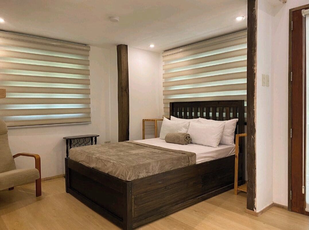 A bedroom with a wooden bed, a chair, and a window with blinds.