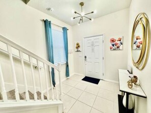 A clean, well-lit hallway with a white staircase, a door with a doormat, and a wall-mounted mirror.