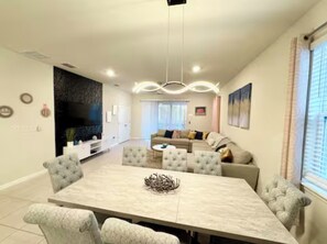 A spacious living area with a large dining table, comfortable seating, a modern entertainment unit, and a cozy seating area with a sofa and cushions. - The Dream Getaway Retreat Near Disney (Davenport)