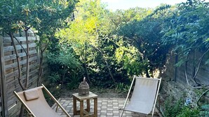A patio area with two wooden lounge chairs and a small table, surrounded by a brick floor and lush greenery. - Renovated 4 Pers Studio with Garden and Private Parking (83270 ST CYR)