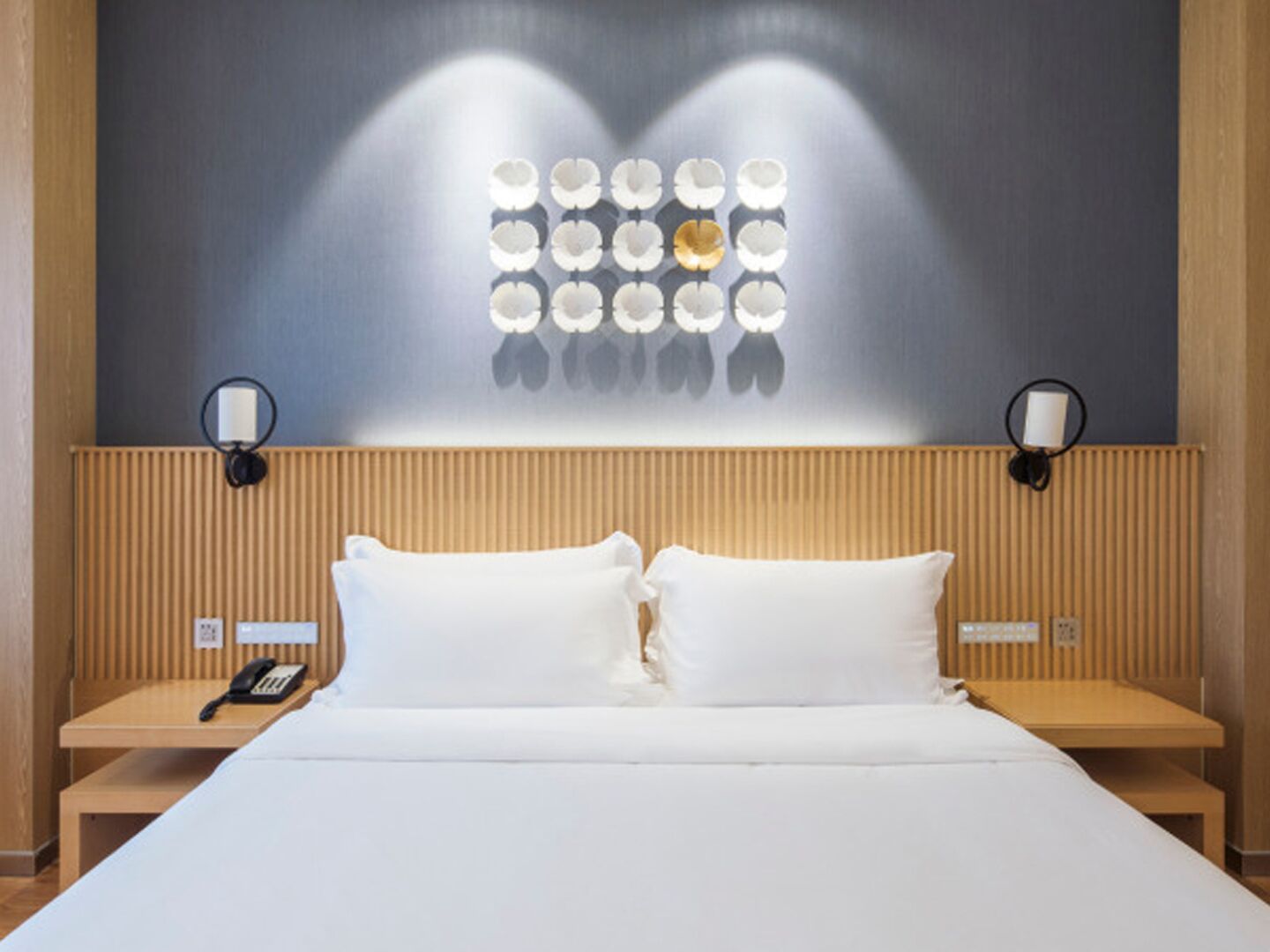 Hotellihuone, jossa on suuri sänky, kaksi yöpöytää, seinään kiinnitetty valaisin ja puhelin toisella yöpöydällä.