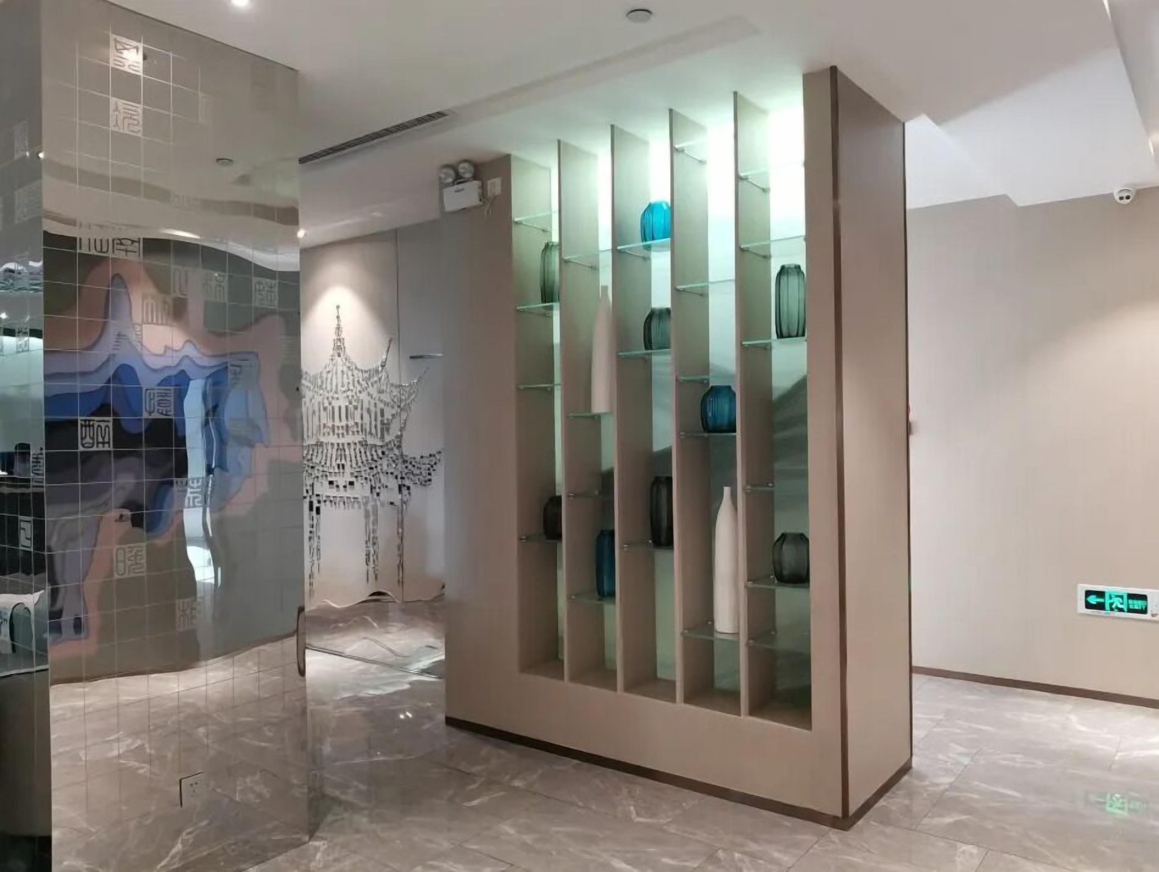 Un interior moderno con un aparador de vidrio, una pared con mosaicos y patrones abstractos, y un piso de mármol.
