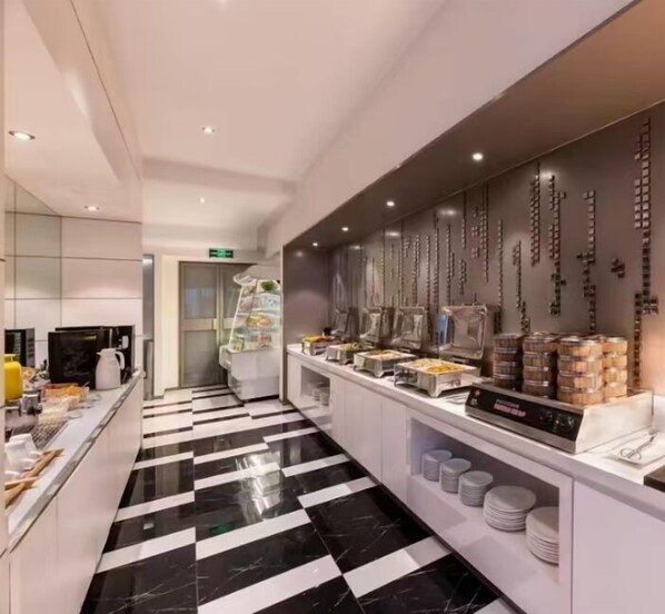 Un lobby moderno de hotel con un mostrador de recepción, un área de buffet con diversas opciones de comida y un suelo a cuadros blanco y negro.