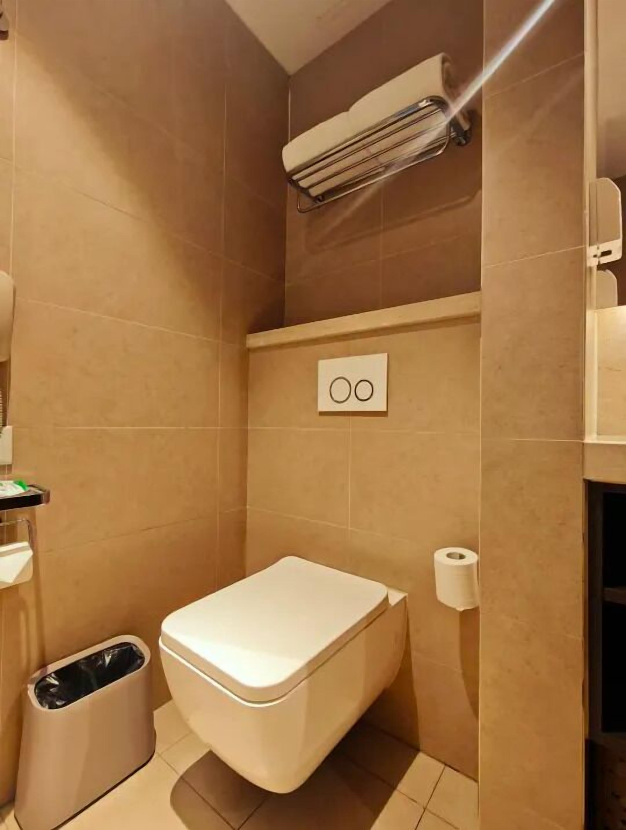 Baño pequeño con inodoro, un bote de basura, toallero y equipo de aire acondicionado.