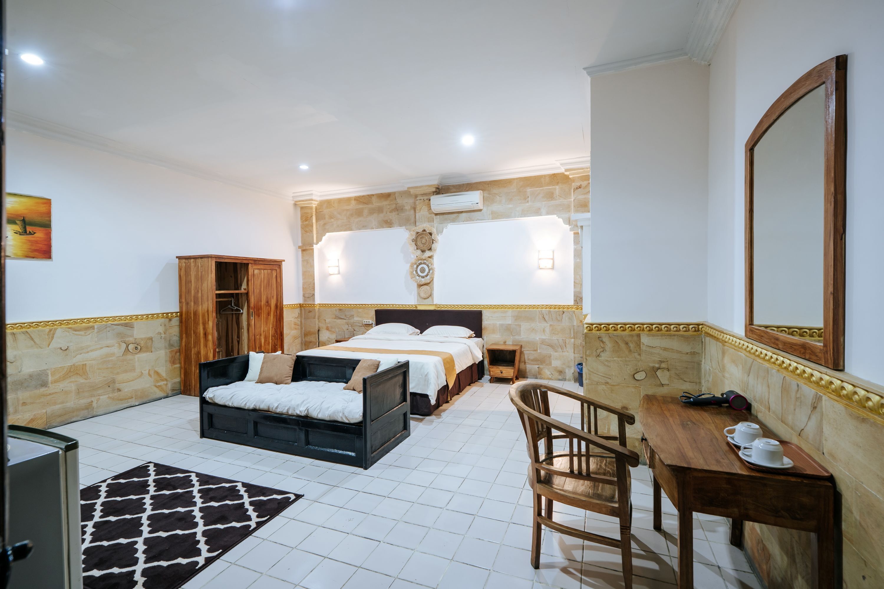 A hotel room with a bed, a desk, a chair, and a small table with cups.