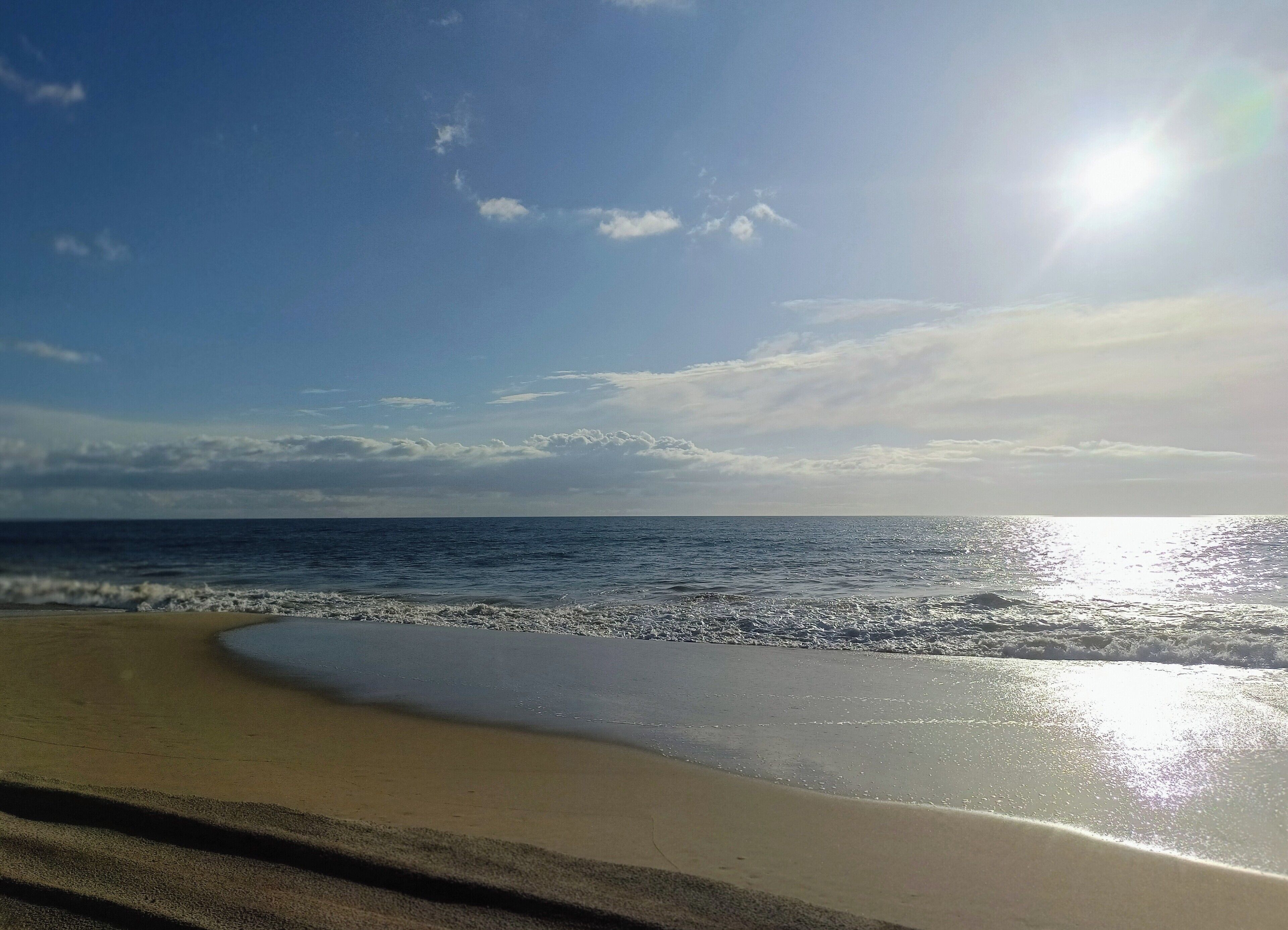 Une plage avec un ciel dégagé et la lumière du soleil se reflétant sur l’eau.