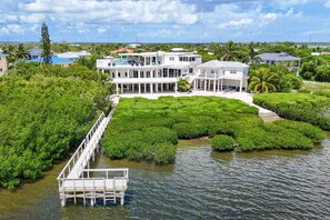 A large white building with multiple levels, surrounded by lush greenery and water.
