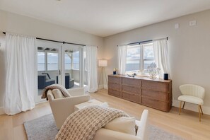 A spacious room with a large window, a sofa, a chair, a wooden cabinet, and a lamp.
