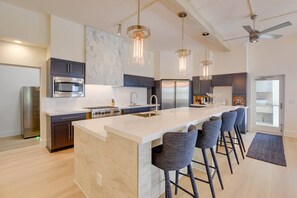 A modern kitchen with a central island, bar stools, stainless steel appliances, pendant lighting, and a ceiling fan.