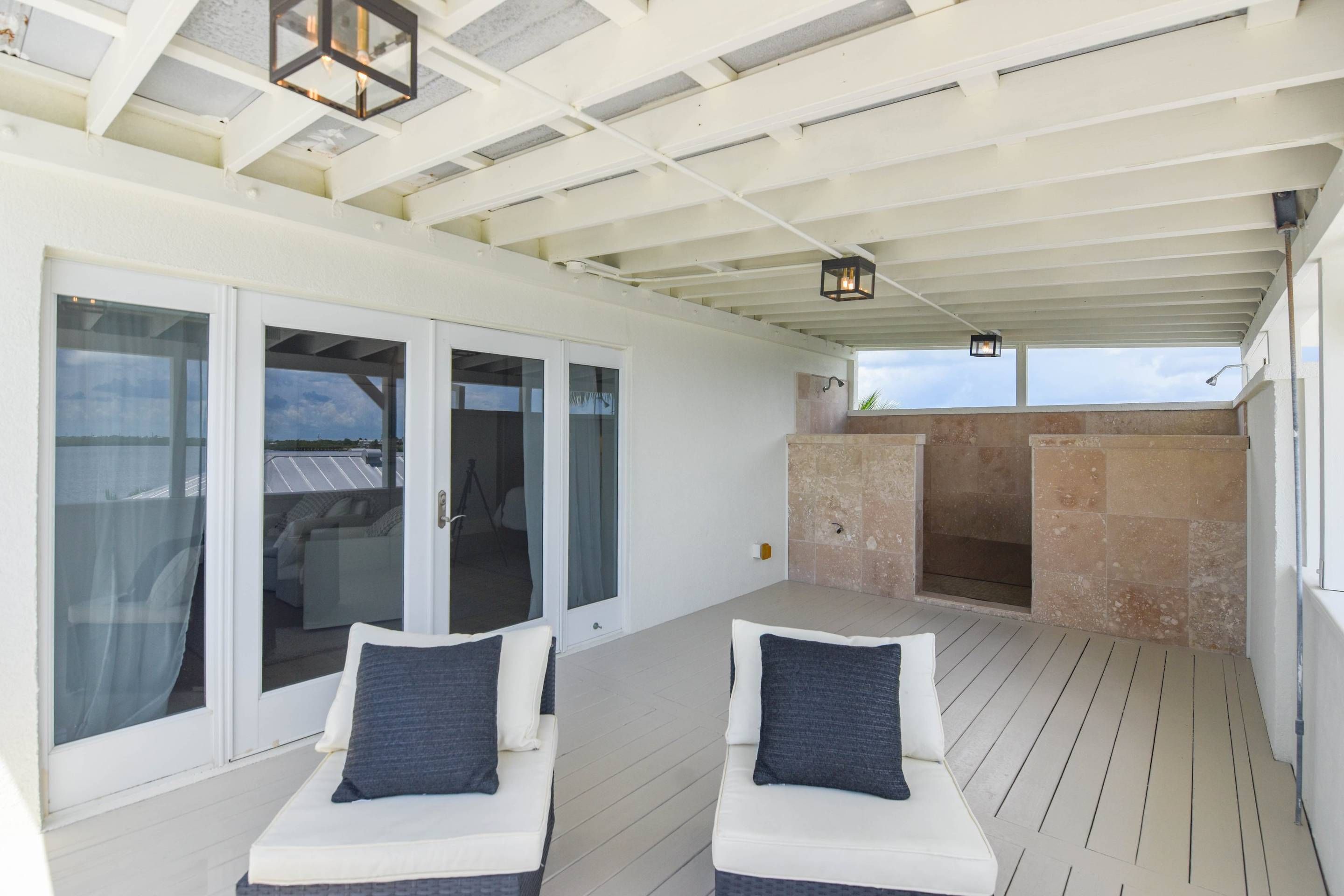 A covered outdoor seating area with two cushioned chairs and a stone fireplace.