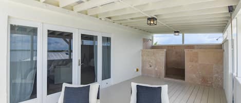 A covered outdoor seating area with two cushioned chairs and a stone fireplace.