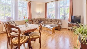 A living room with a sofa, a coffee table, a TV, and a dining table with chairs.