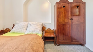 A bedroom with a bed, a wooden wardrobe with heart-shaped cutouts, and a white arched ceiling.