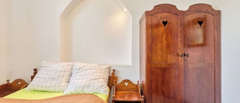 A bedroom with a bed, a wooden wardrobe with heart-shaped cutouts, and a white arched ceiling.