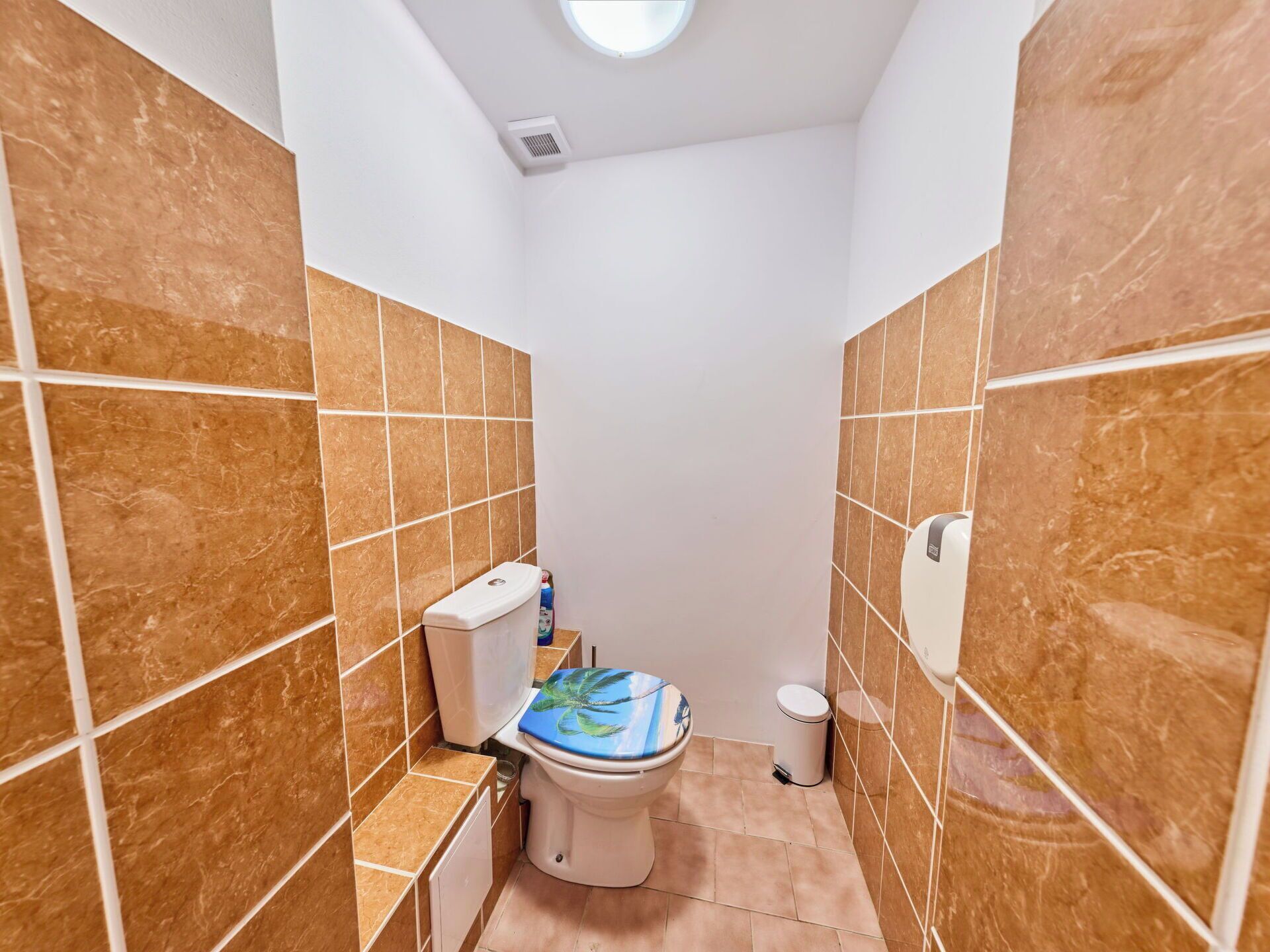 A compact bathroom with a toilet, a hand dryer, and a trash bin.