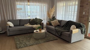 A living room with two grey sofas, a round coffee table, and a large window with sheer curtains.