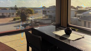 A balcony with a view of a residential area, a table with a vase, and a chair.