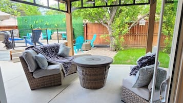 Un patio exterior con mobiliario de mimbre, una mesa redonda y una estructura de pérgola.