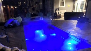 A heated outdoor swimming pool with blue lighting, surrounded by a deck and outdoor furniture.