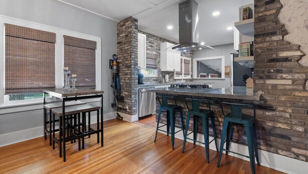 A modern kitchen with a brick accent wall, a central island with bar stools, and a dining area with a wooden table and chairs.
