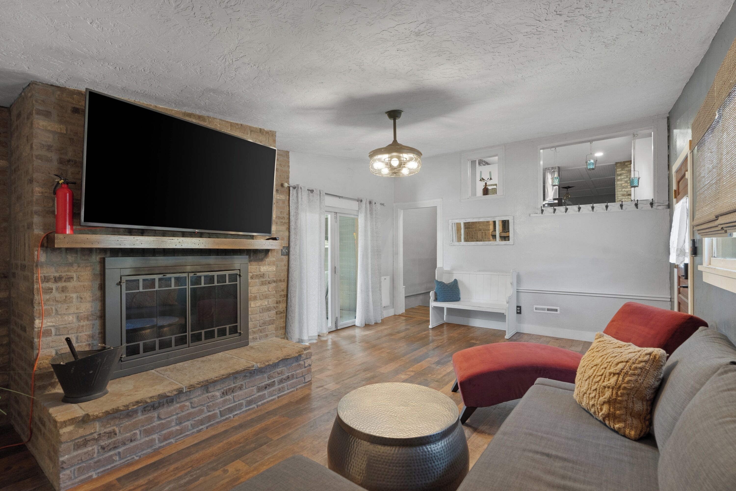 Een woonkamer met een open haard, een flatscreen-tv, een rode bank en een ronde houten tafel.