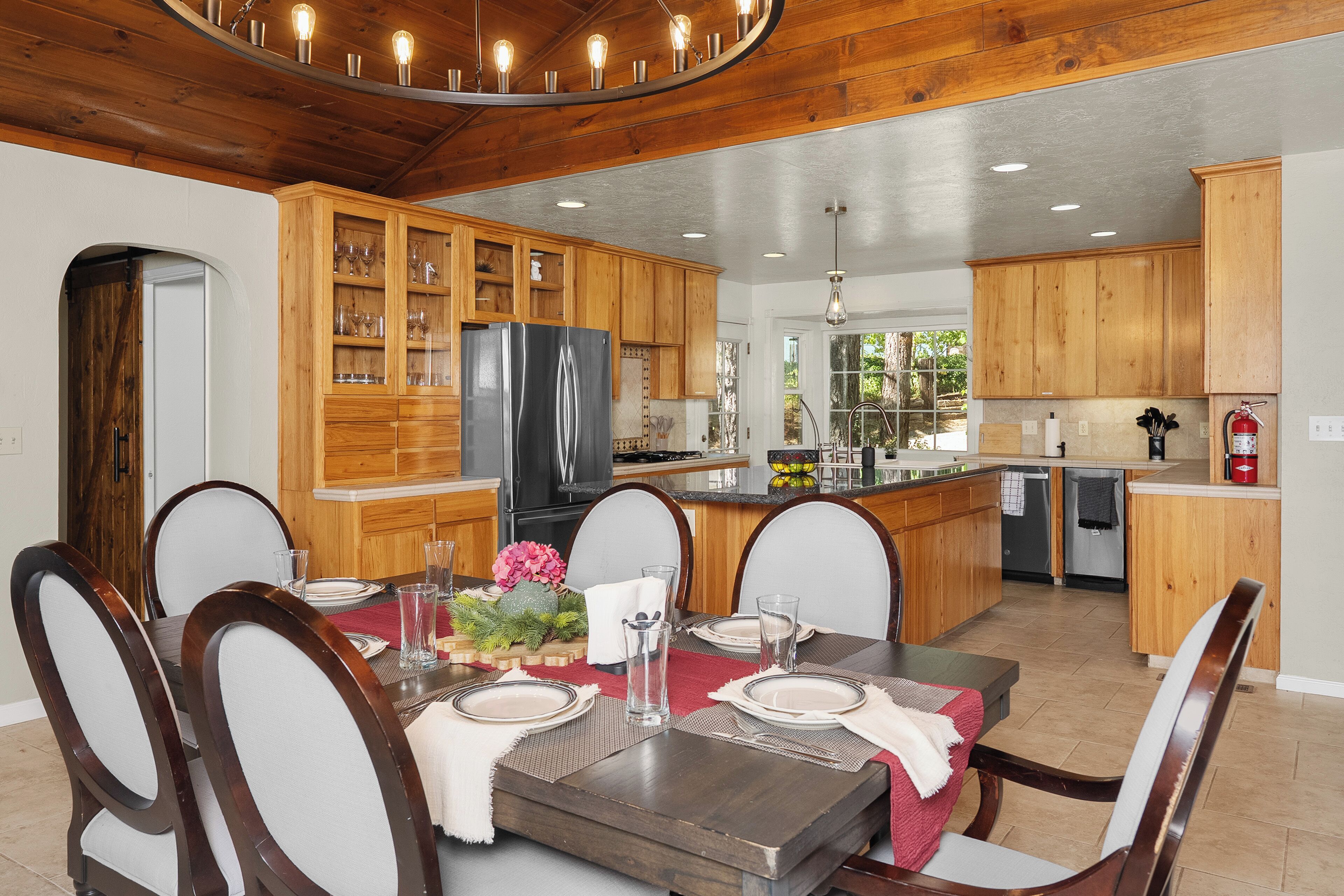 A modern kitchen with wooden cabinets, a stainless steel refrigerator, and a dining area with a wooden table and chairs.